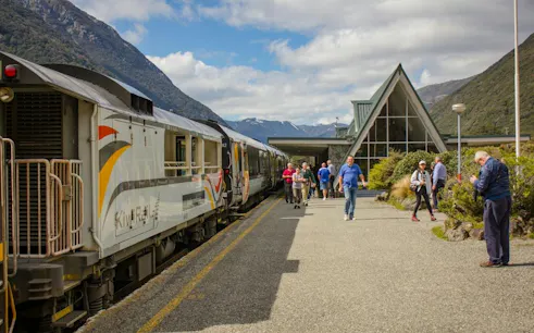 TranzAlpine train at Arthur’s Pass station with passengers, mountains in background, Christchurch tour.