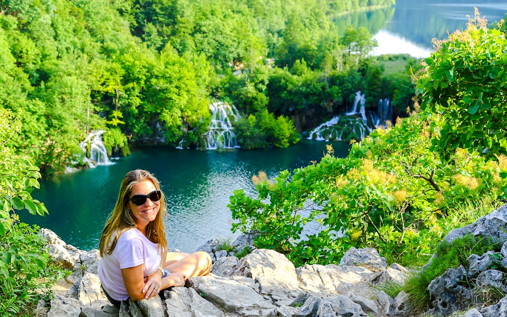 Tourist sitting on a rock overlooking waterfalls at Plitvice Lakes, Croatia.
