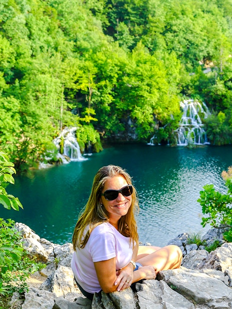 Tourist sitting on a rock overlooking waterfalls at Plitvice Lakes, Croatia.