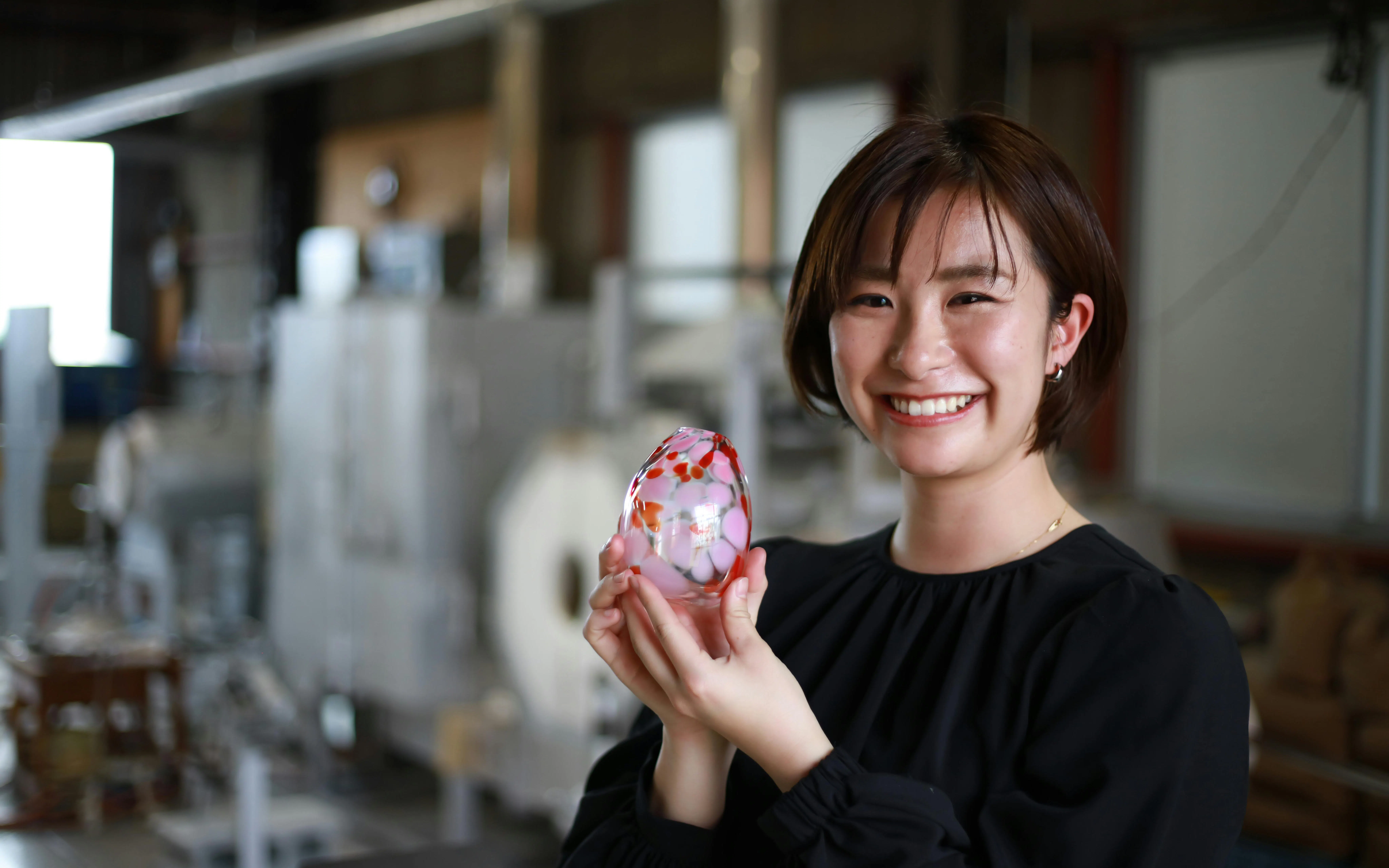 Woman smiling while holding a colorful glass container in a workshop.