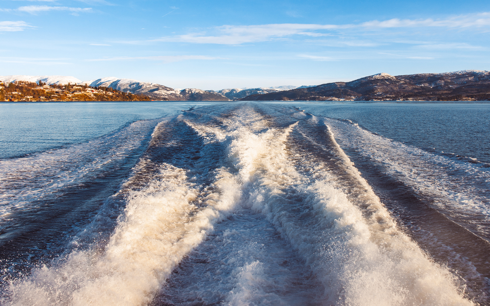 Wake trail on Mostraumen Fjord Cruise with snowy mountains in the background.