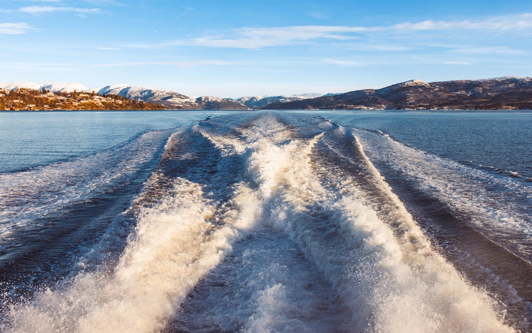 Wake trail on Mostraumen Fjord Cruise with snowy mountains in the background.