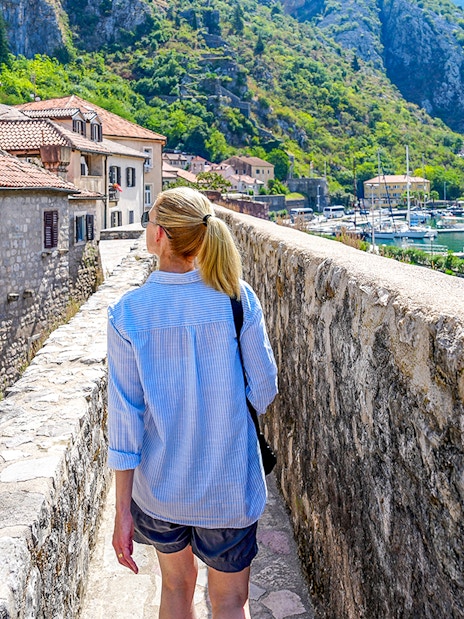 Guest walking along Kotor's historic walls with view of bay and boats during Montenegro tour.