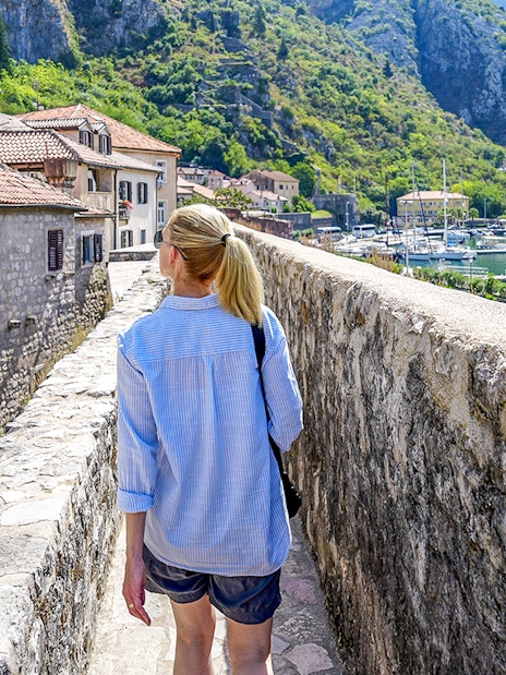 Guest walking along Kotor's historic walls with view of bay and boats during Montenegro tour.