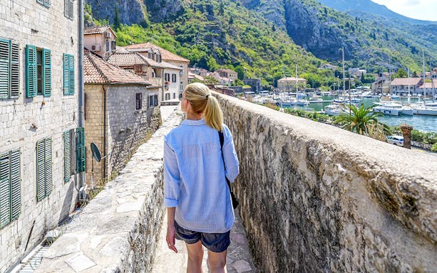 Guest walking along Kotor's historic walls with view of bay and boats during Montenegro tour.