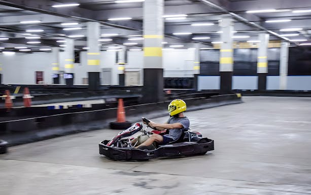 Person driving go-kart on indoor track in Bangkok.