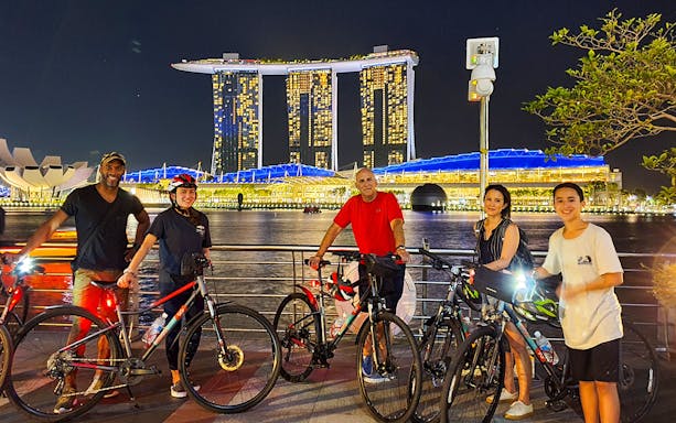Group on bikes with Marina Bay Sands illuminated at night in Singapore.