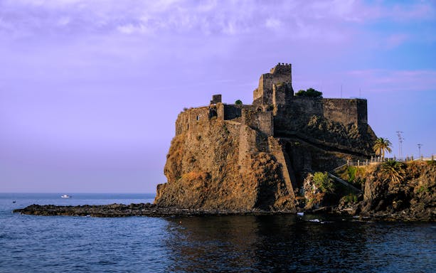 Aci Castello castle on a rocky cliff by the sea, part of the Riviera of the Cyclops tour from Catania.
