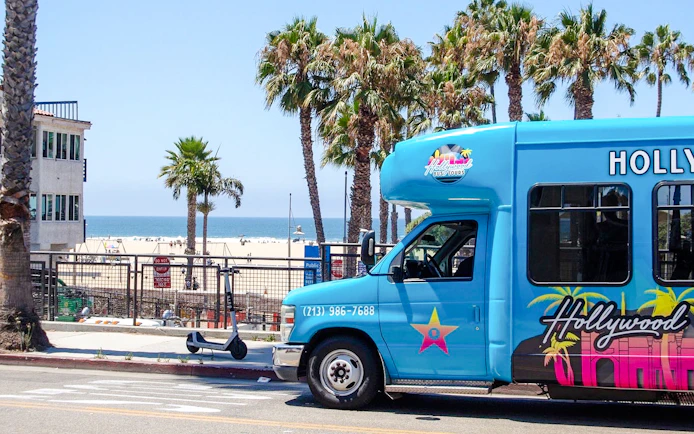 Hollywood bus tour vehicle near Los Angeles beach with palm trees.