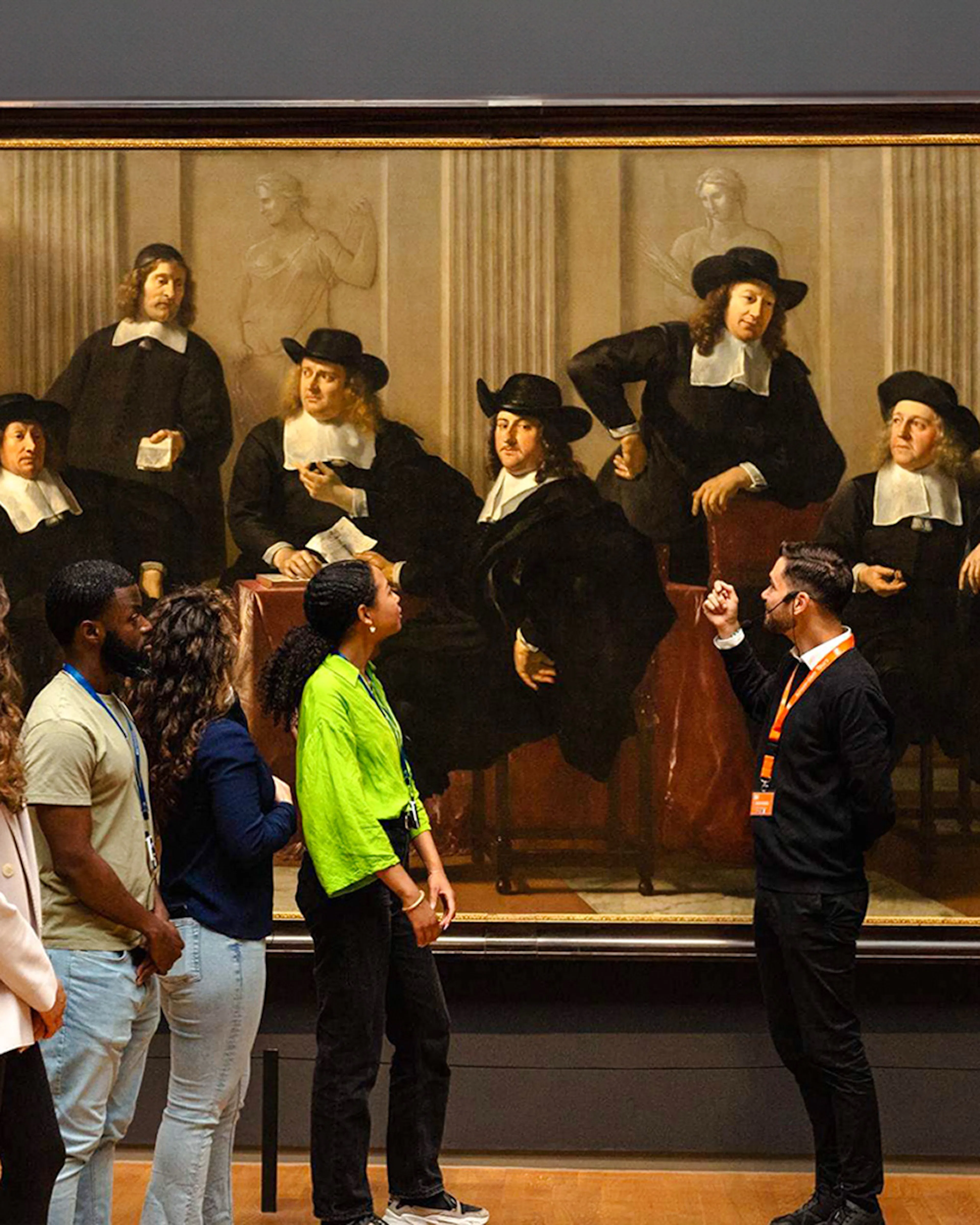 Visitors observing a large historical painting at the Rijksmuseum, Amsterdam.