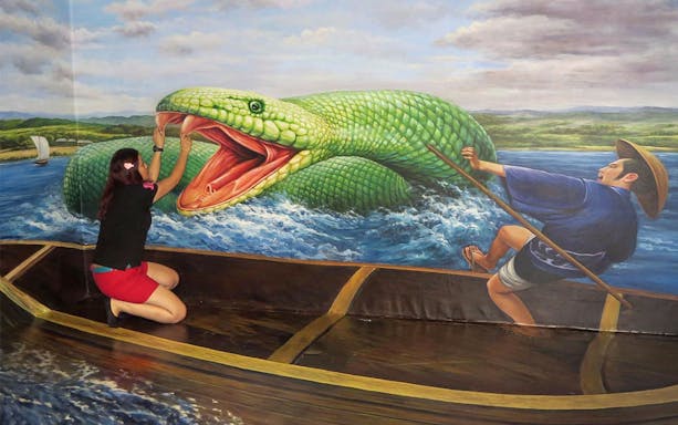 Person interacting with 3D art of a giant snake at Alive 3D Art Gallery.