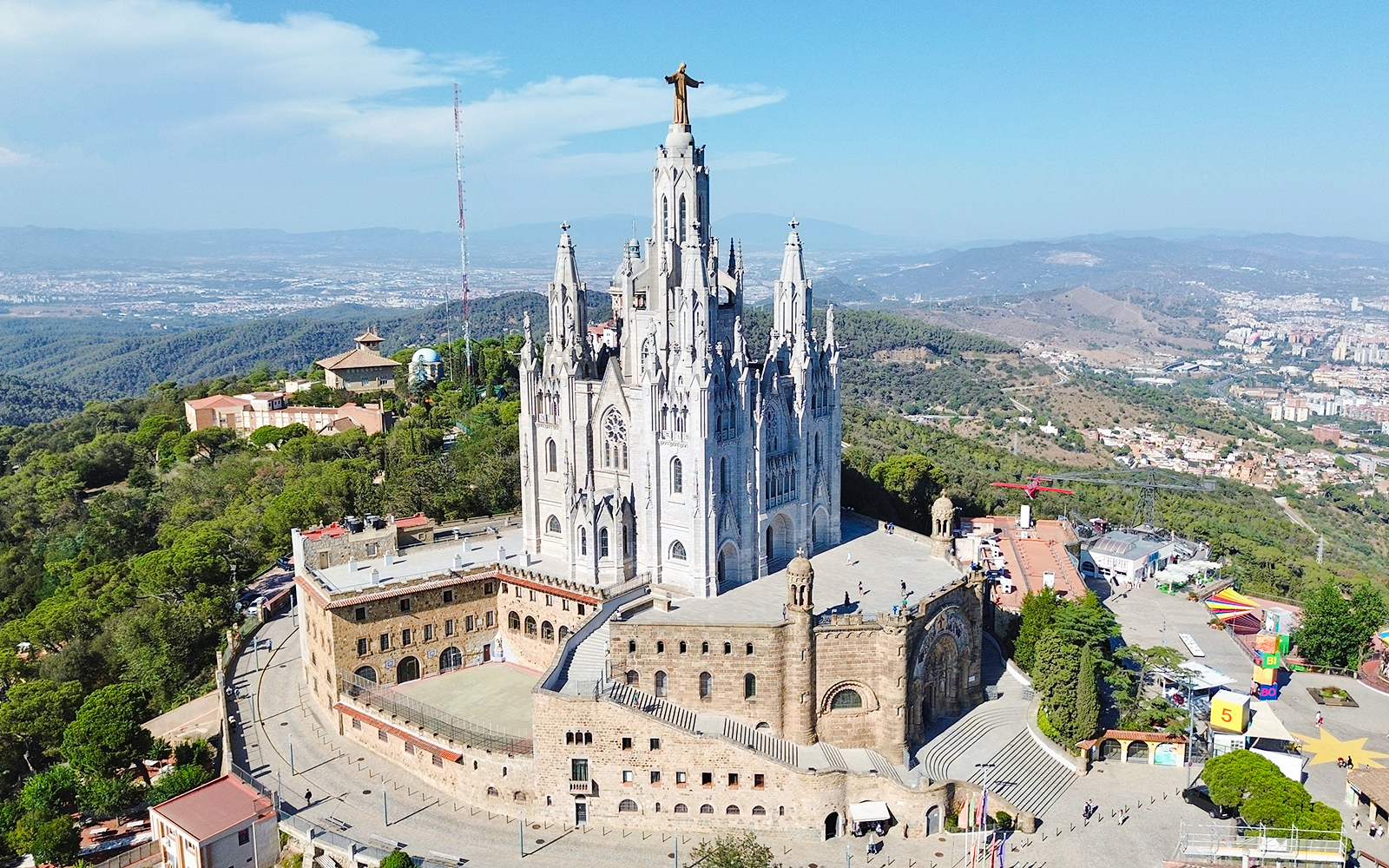 Aerial view of the Temple of the Sacred Heart of Jesus in Barcelona, surrounded by lush hills.