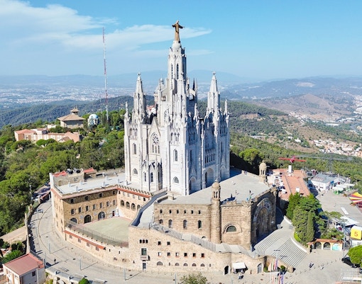 Aerial view of the Temple of the Sacred Heart of Jesus in Barcelona, surrounded by lush hills.