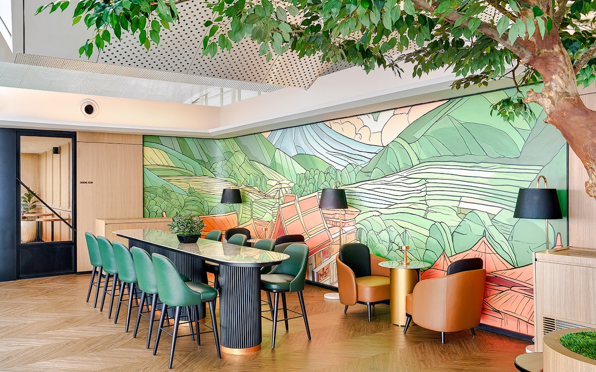 Lounge interior with green chairs, mural of mountains, and potted plants.