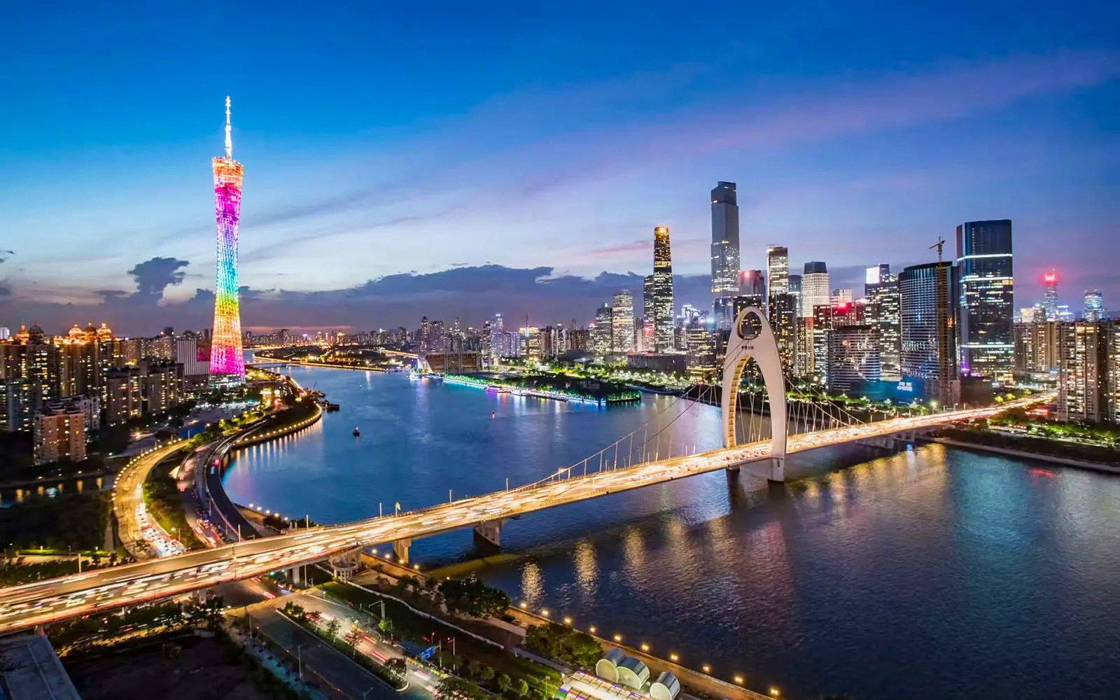 Canton Tower illuminated at night beside a river with city skyline and bridge in Guangzhou.