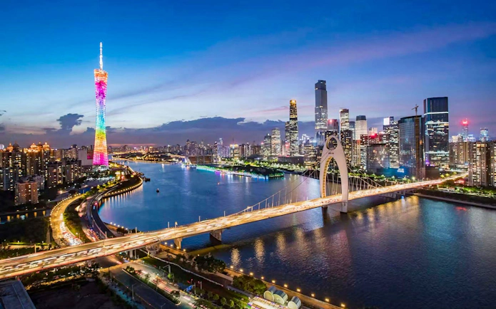 Canton Tower illuminated at night beside a river with city skyline and bridge in Guangzhou.
