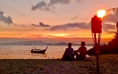 Longtail boat at sunset with people on Krabi beach, torch lit, 7 Islands Tour.