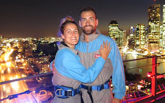 Couple on Brisbane Story Bridge during twilight climb with city lights in background.