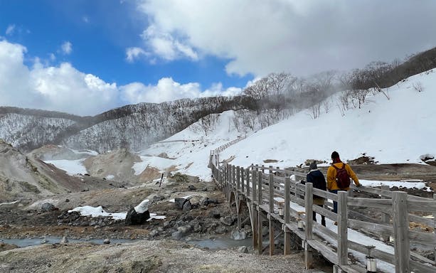 Visitors walking on a wooden path through snowy Hell Valley in Noboribetsu, Japan.