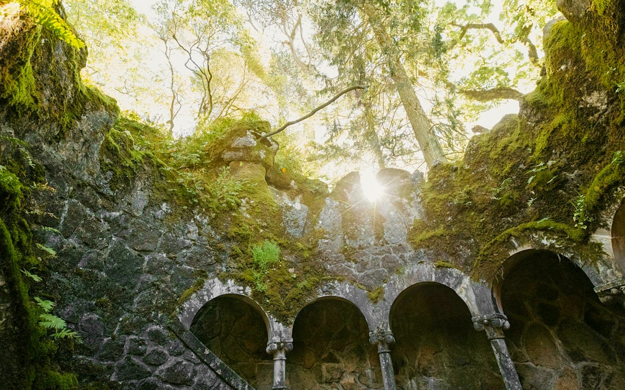 Quinta da Regaleira well with sunlight filtering through moss-covered arches.