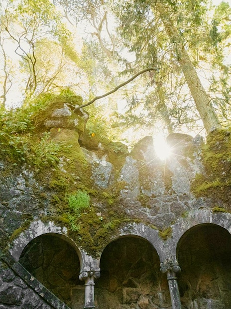 Quinta da Regaleira well with sunlight filtering through moss-covered arches.