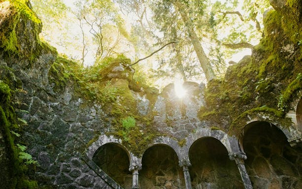 Quinta da Regaleira well with sunlight filtering through moss-covered arches.