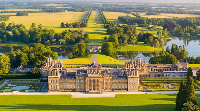 Aerial view of Blenheim Palace with expansive gardens and surrounding countryside in Oxfordshire, England.