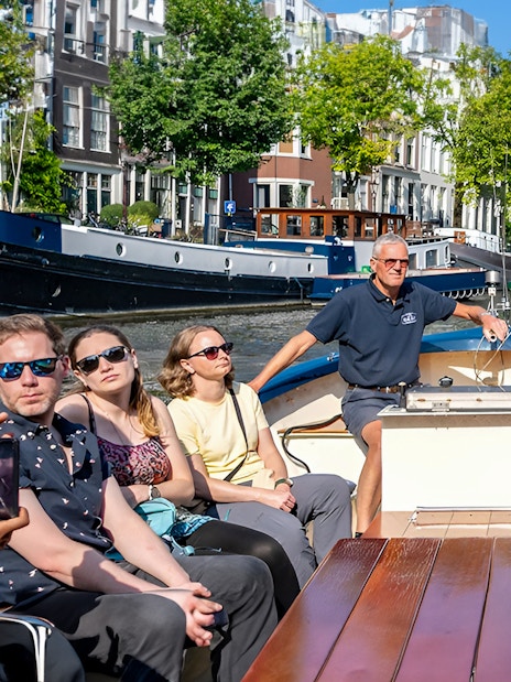 Small open boat with tourists cruising Amsterdam canal, view of Montelbaanstoren tower.
