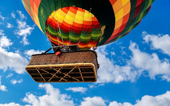 Hot air balloon ascending over Luxor with colorful canopy against blue sky.