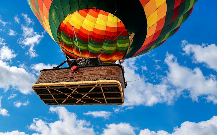 Hot air balloon ascending over Luxor with colorful canopy against blue sky.