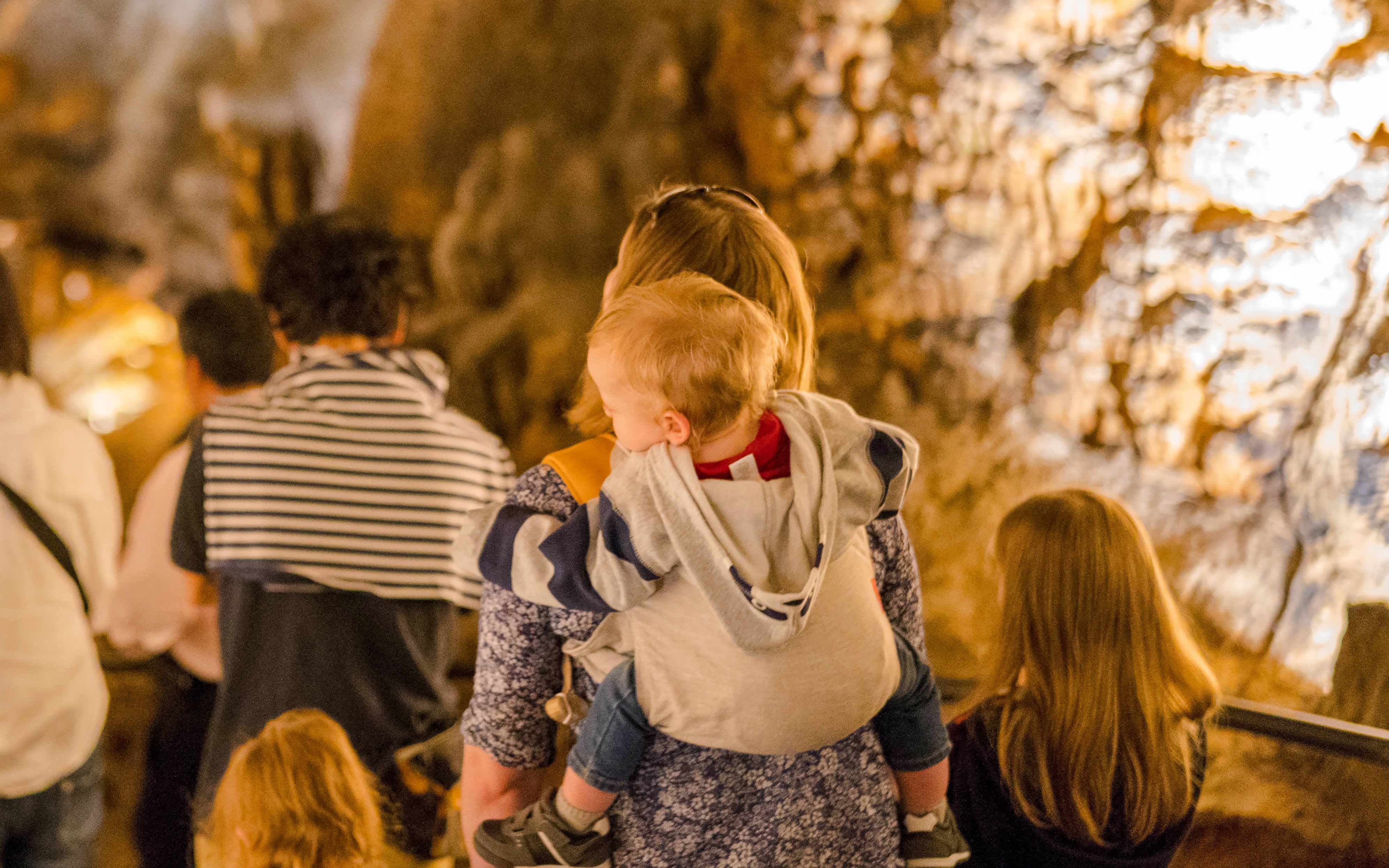 Mother carrying child in a cave tour with other visitors.