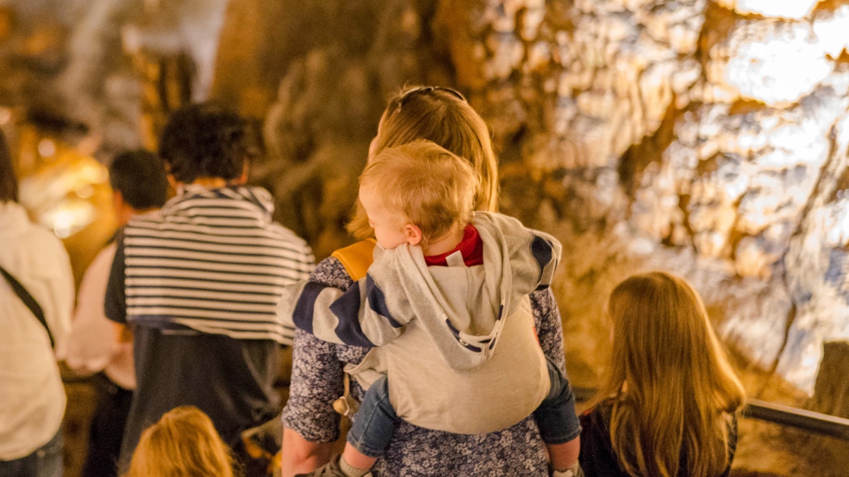 Mother carrying child in a cave tour with other visitors.