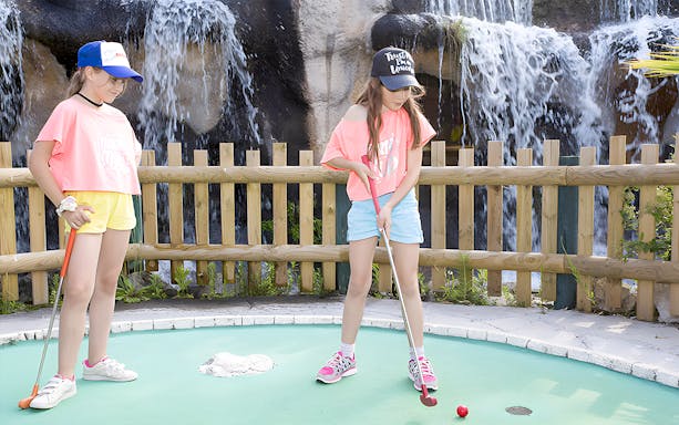 Kids playing mini-golf near a waterfall at an adventure golf course.