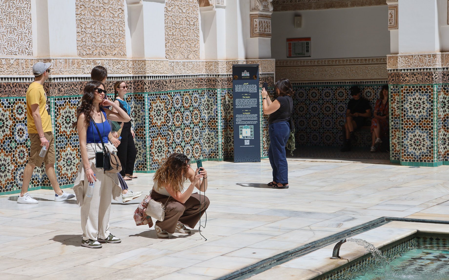 Visitors exploring the intricate tilework at Ben Youssef Medersa, Marrakech.