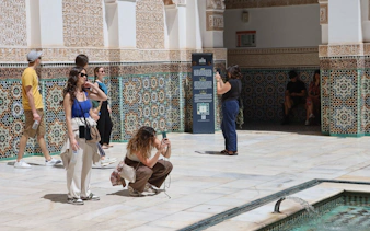 Visitors exploring the intricate tilework at Ben Youssef Medersa, Marrakech.