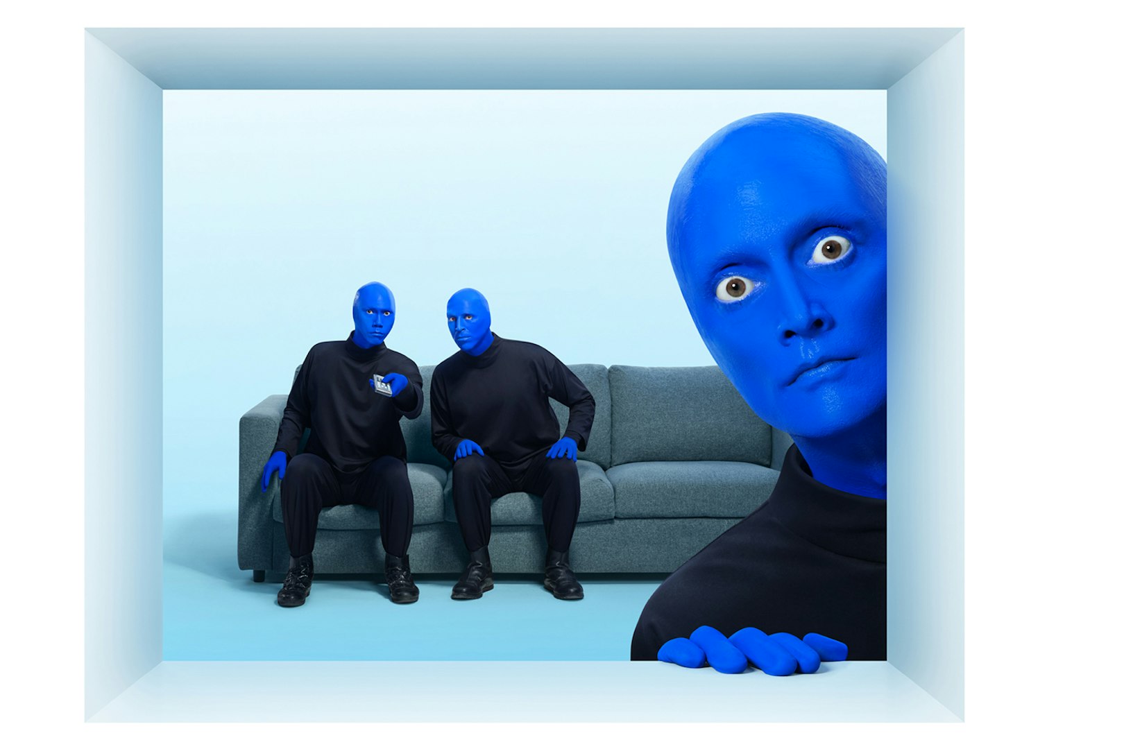 Blue Man Group members in blue makeup sitting on a couch with one peeking from the side.