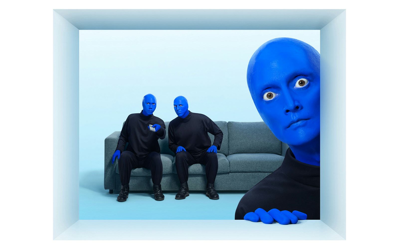 Blue Man Group members sitting on a couch with one peeking from the side.