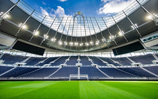 Tottenham Hotspur Stadium interior view with empty seats and green pitch.