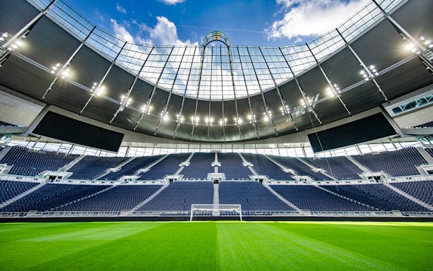 Tottenham Hotspur Stadium interior with empty seats and green pitch.
