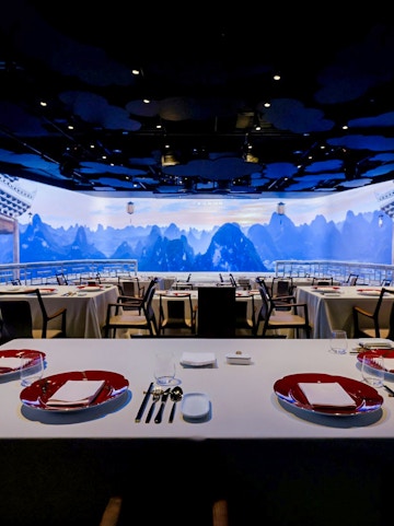 Dining tables set in an immersive Chinese restaurant with mountain landscape backdrop.
