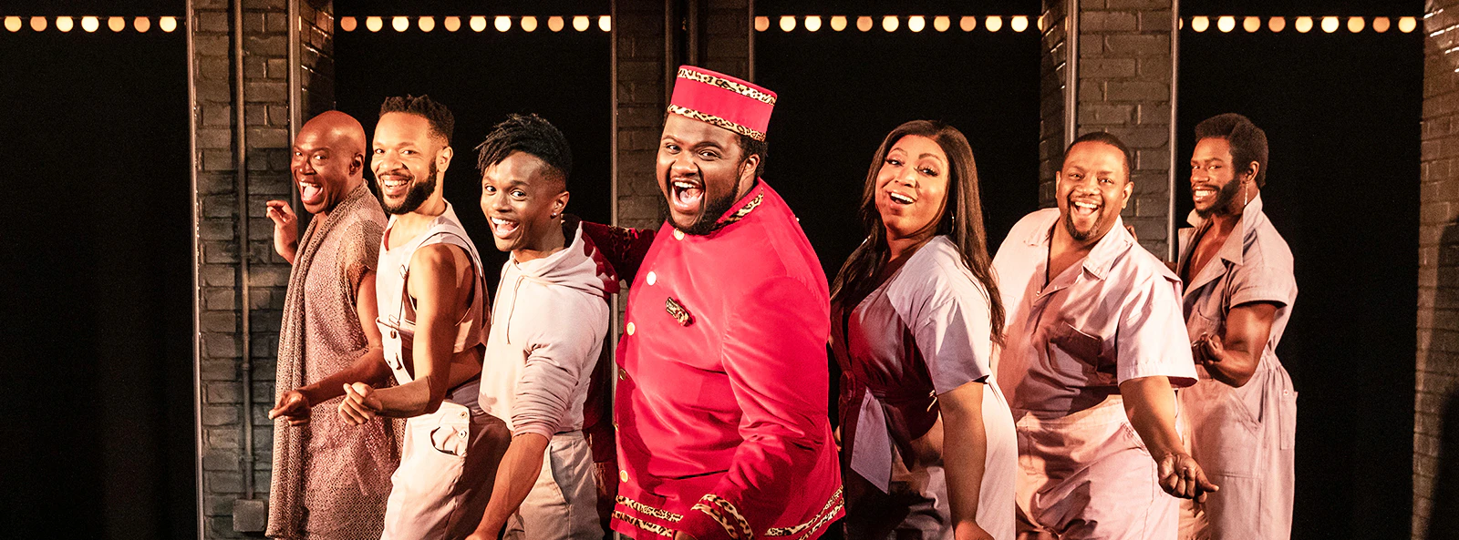 Cast of "A Strange Loop" performing on stage in vibrant costumes.