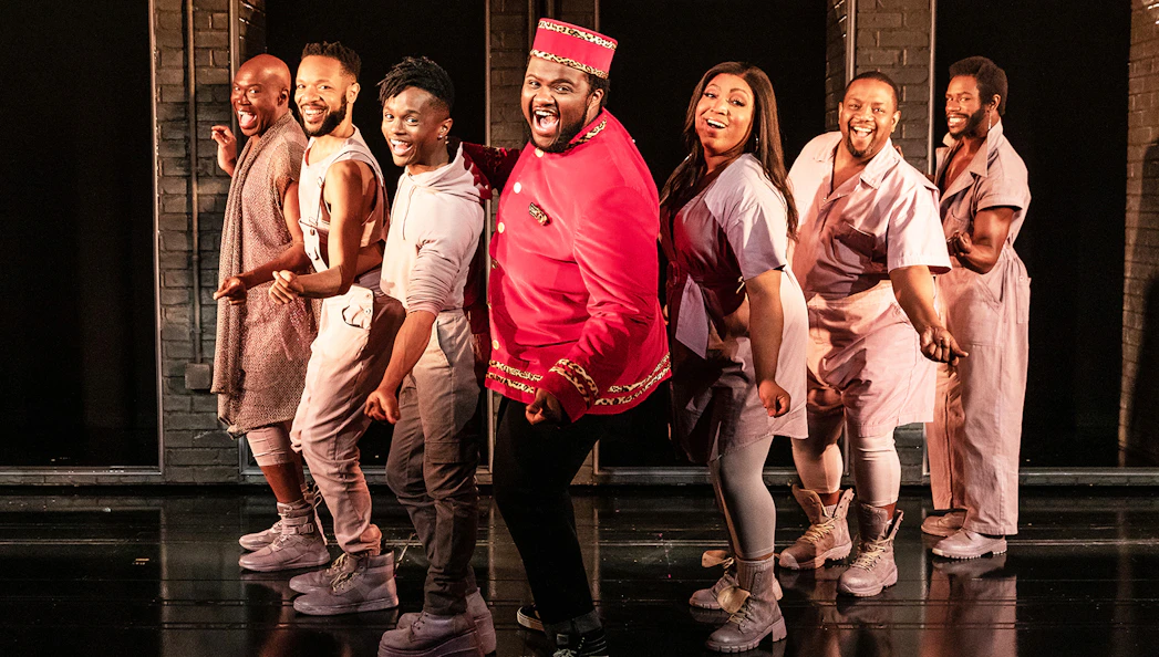 Cast of "A Strange Loop" performing on stage in vibrant costumes.