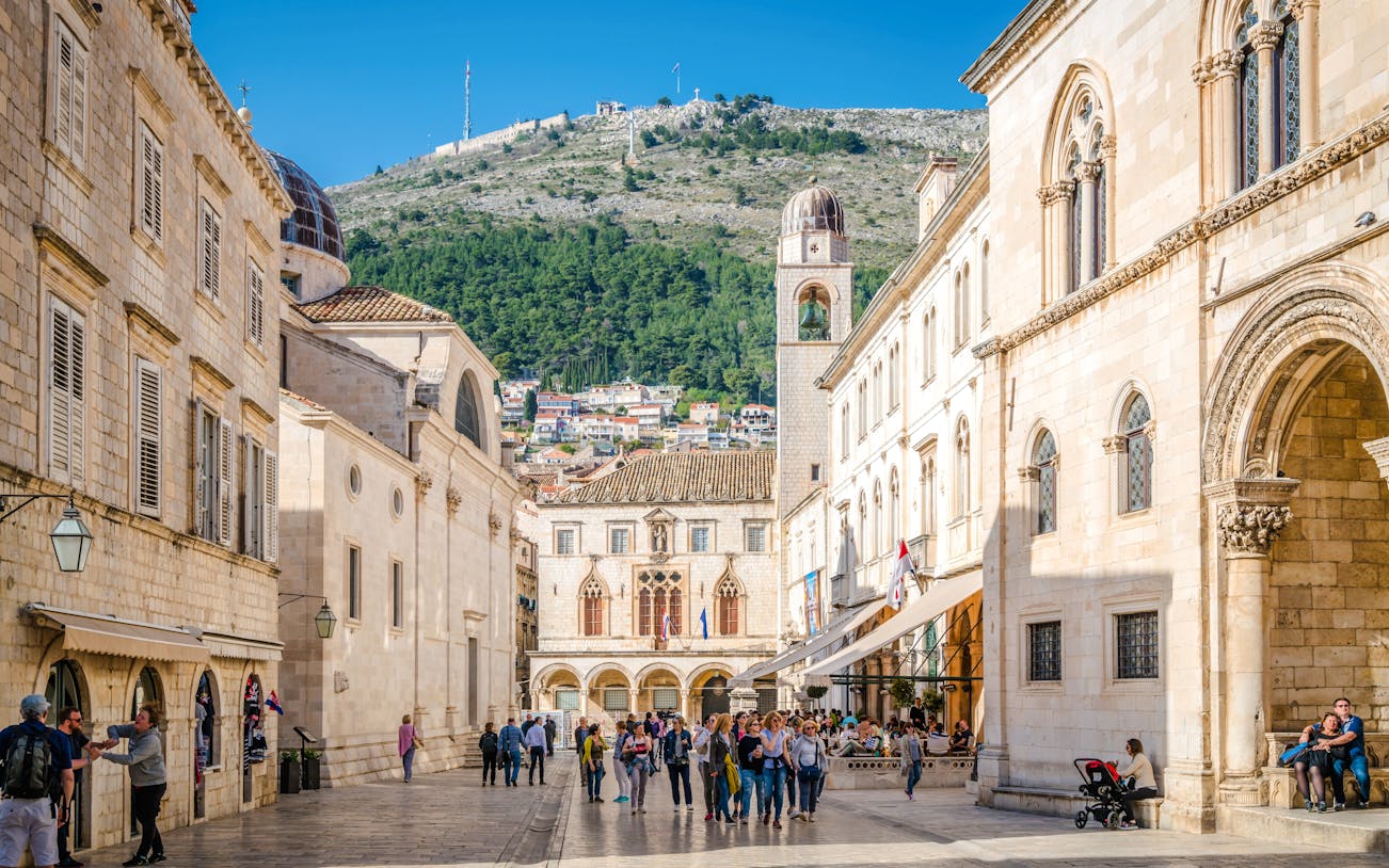 Sponza Palace and Bell Tower in Dubrovnik with people walking in the square.