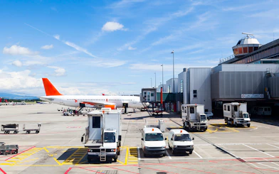 Airplane on runway at Geneva Airport with service vehicles nearby.