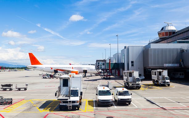 Airplane on runway at Geneva Airport with service vehicles nearby.