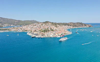 Cruise ship sailing near Poros island with coastal town and boats in view.