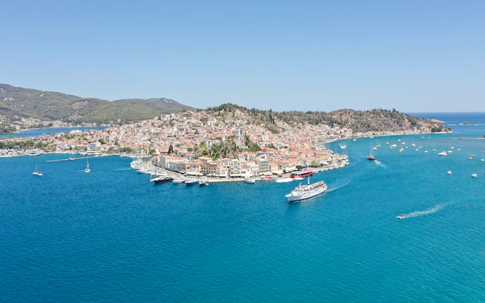 Cruise ship sailing near Poros island with coastal town and boats in view.