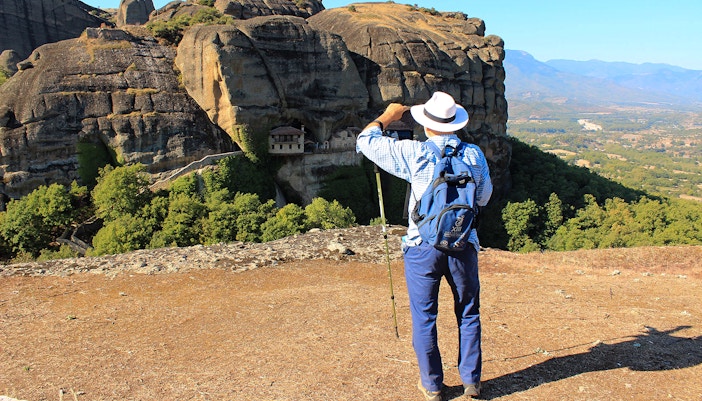 Guest hiking with view of Meteora rock formations and monastery in Greece.