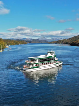 Boat cruising on Lake Windermere in the Lake District, surrounded by hills and clear skies.