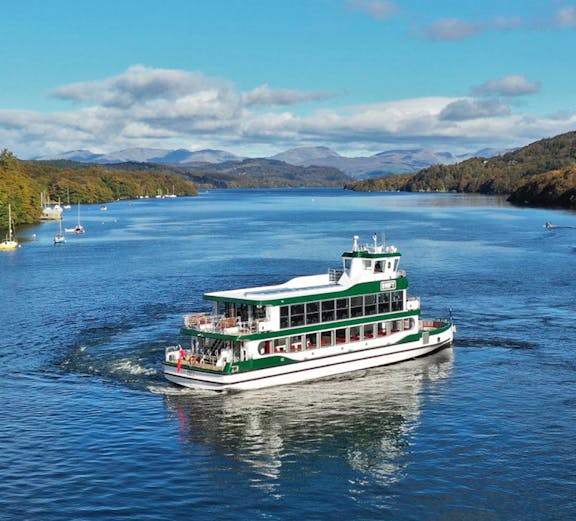 Boat cruising on Lake Windermere in the Lake District, surrounded by hills and clear skies.